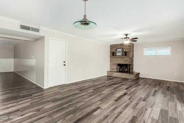 unfurnished living room with wood finished floors, visible vents, ceiling fan, a stone fireplace, and ornamental molding