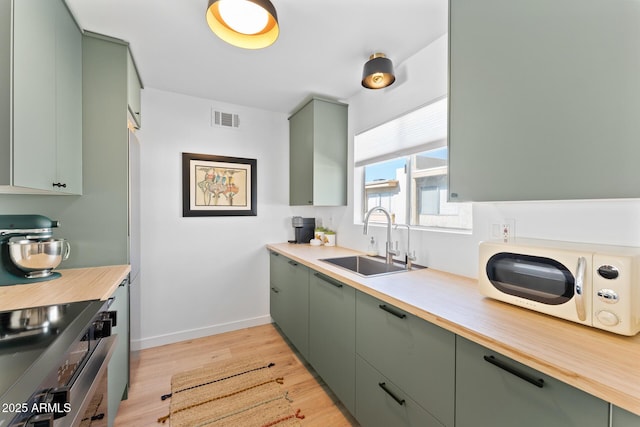 kitchen with stainless steel electric stove, sink, light hardwood / wood-style flooring, and green cabinetry