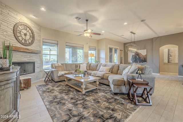 living room featuring a fireplace, light wood-type flooring, and ceiling fan with notable chandelier