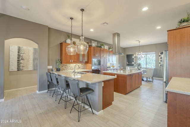 kitchen featuring kitchen peninsula, a kitchen breakfast bar, island exhaust hood, sink, and hanging light fixtures