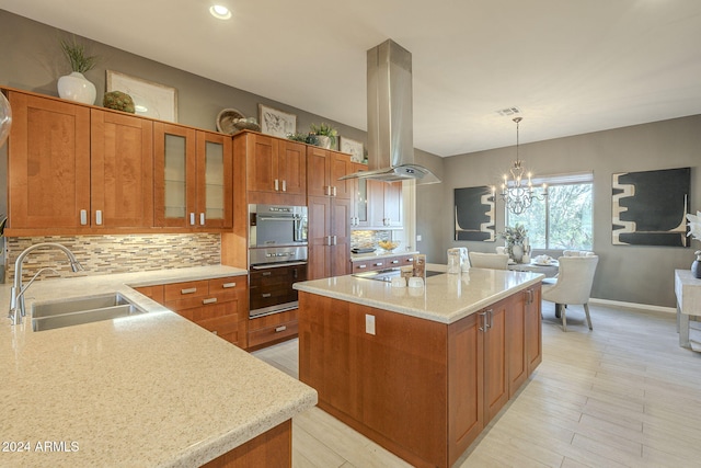 kitchen featuring light stone counters, island range hood, sink, pendant lighting, and an inviting chandelier