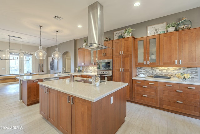 kitchen featuring an island with sink, appliances with stainless steel finishes, island range hood, light stone counters, and kitchen peninsula