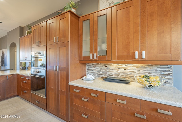 kitchen featuring light stone countertops, backsplash, and double oven