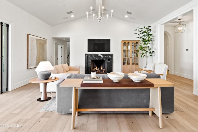 living room with light hardwood / wood-style floors, a high end fireplace, lofted ceiling, and an inviting chandelier