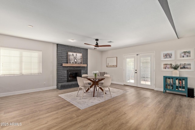 dining area with visible vents, baseboards, light wood-style floors, french doors, and a brick fireplace