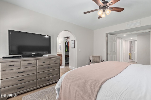 bedroom with visible vents, a walk in closet, arched walkways, light wood finished floors, and baseboards