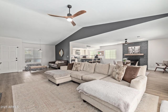 living area featuring a brick fireplace, baseboards, lofted ceiling, wood finished floors, and a ceiling fan