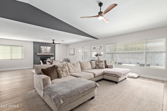 living room with a brick fireplace, vaulted ceiling, a ceiling fan, and light wood finished floors