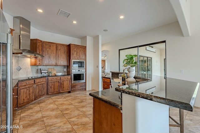 28423 N 139th St, Scottsdale, AZ 85262 - kitchen featuring visible vents, stainless steel appliances, arched walkways, wall chimney range hood, and brown cabinetry
