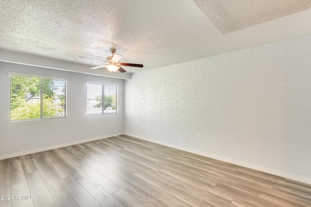 unfurnished room featuring ceiling fan, a textured ceiling, brick wall, baseboards, and light wood finished floors