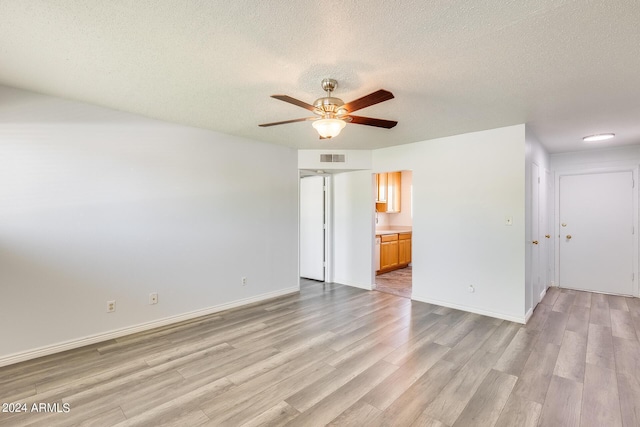 spare room featuring light wood-style floors, ceiling fan, visible vents, and a textured ceiling