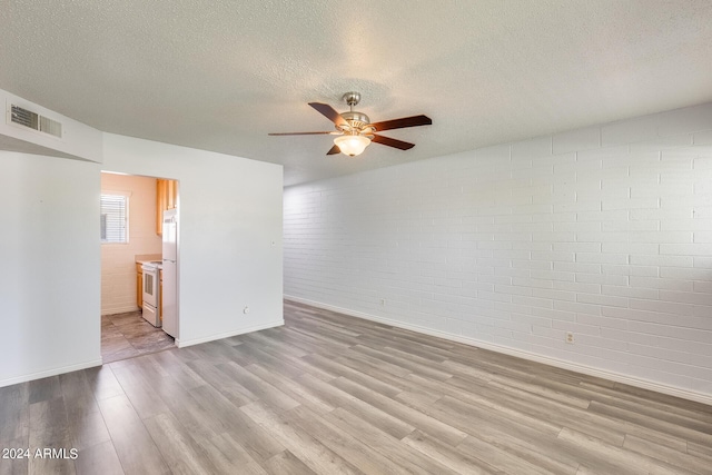 unfurnished room with visible vents, brick wall, ceiling fan, wood finished floors, and a textured ceiling