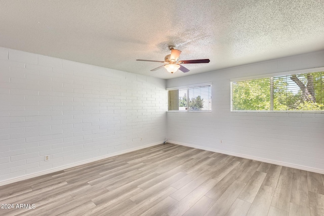 empty room featuring light wood finished floors, baseboards, a ceiling fan, brick wall, and a textured ceiling