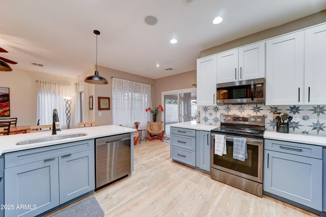 kitchen featuring a sink, stainless steel appliances, light wood-style floors, light countertops, and decorative backsplash