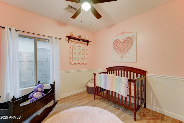 bedroom featuring visible vents, baseboards, a nursery area, and wood finished floors