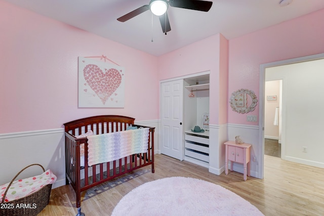 bedroom with a closet, a crib, a ceiling fan, and wood finished floors