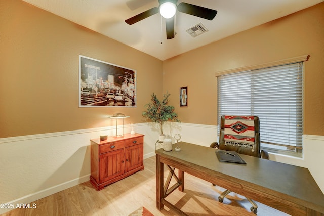 office space with visible vents, light wood-style flooring, a ceiling fan, and a wainscoted wall