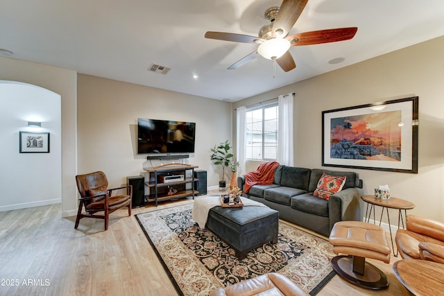 living room featuring visible vents, arched walkways, light wood-style floors, and baseboards