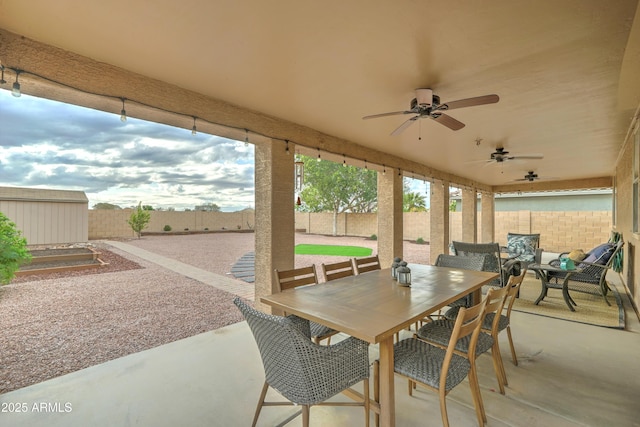 view of patio / terrace with an outbuilding, outdoor dining space, a fenced backyard, a shed, and ceiling fan