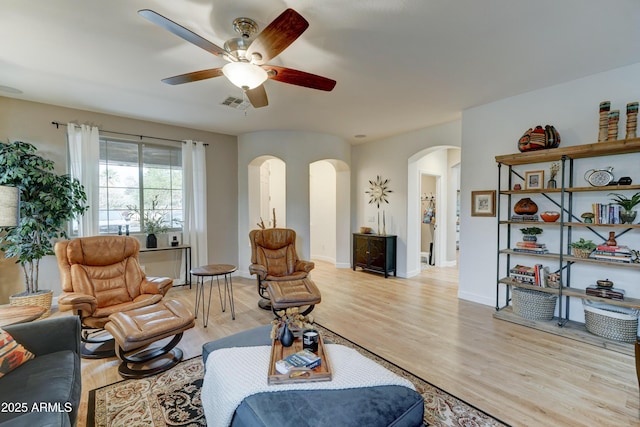 living area featuring arched walkways, visible vents, baseboards, and light wood-style floors