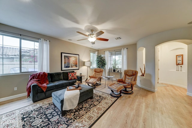 living room featuring visible vents, arched walkways, light wood finished floors, baseboards, and ceiling fan