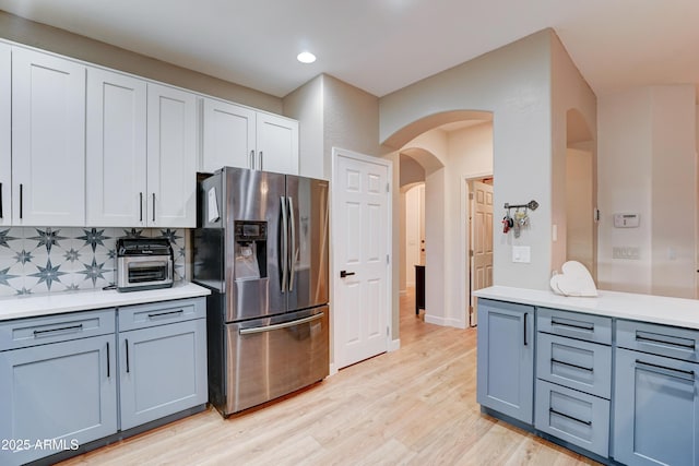 kitchen featuring light wood finished floors, arched walkways, decorative backsplash, light countertops, and stainless steel fridge