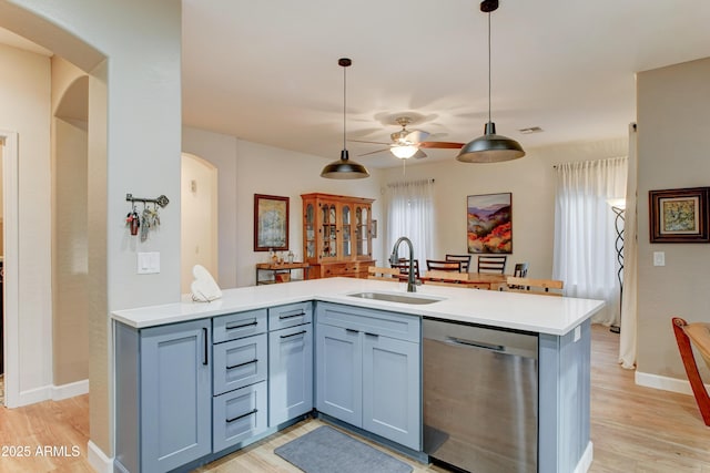 kitchen featuring a sink, stainless steel dishwasher, arched walkways, light wood-style floors, and light countertops