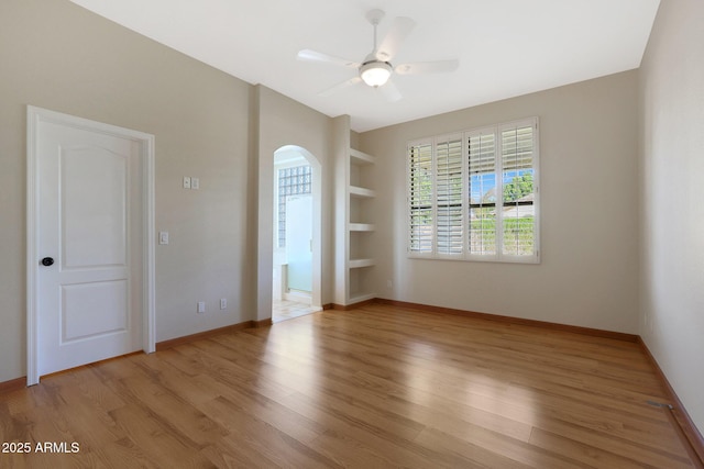 spare room featuring built in shelves, ceiling fan, and light wood-type flooring