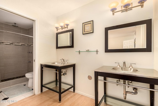 bathroom featuring hardwood / wood-style flooring, toilet, a tile shower, and sink