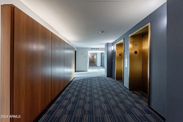 corridor with elevator and dark colored carpet