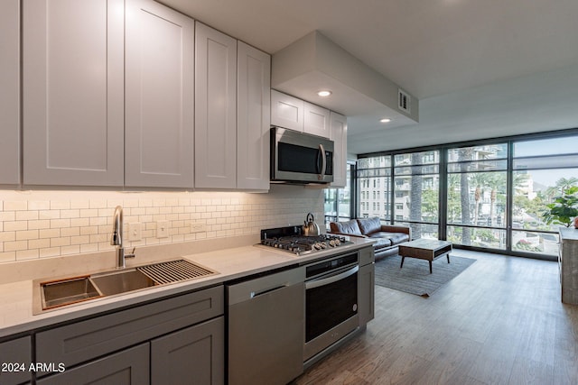 kitchen with decorative backsplash, appliances with stainless steel finishes, floor to ceiling windows, light wood-type flooring, and sink