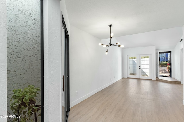 empty room with a notable chandelier, light wood-type flooring, and french doors