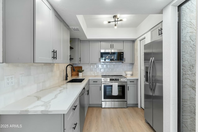 kitchen featuring sink, gray cabinetry, stainless steel appliances, light stone counters, and light wood-type flooring