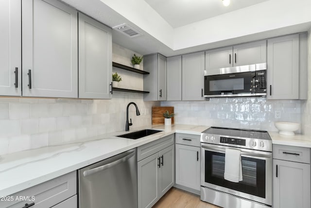 kitchen with sink, gray cabinets, stainless steel appliances, light stone countertops, and backsplash