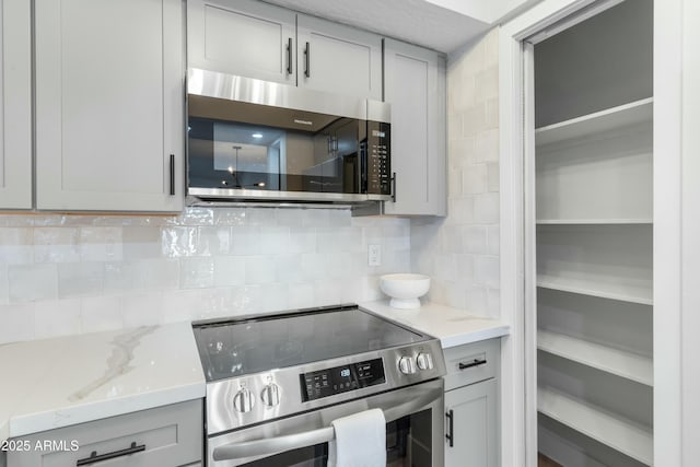 kitchen with gray cabinetry, light stone counters, tasteful backsplash, and appliances with stainless steel finishes