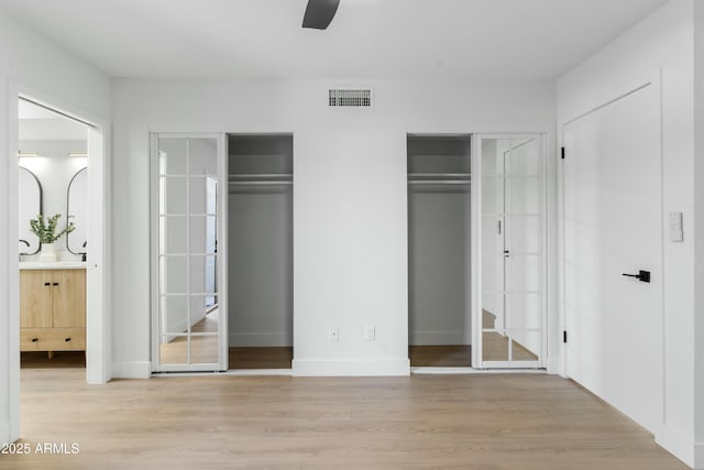 unfurnished bedroom featuring ceiling fan, connected bathroom, two closets, and light hardwood / wood-style floors