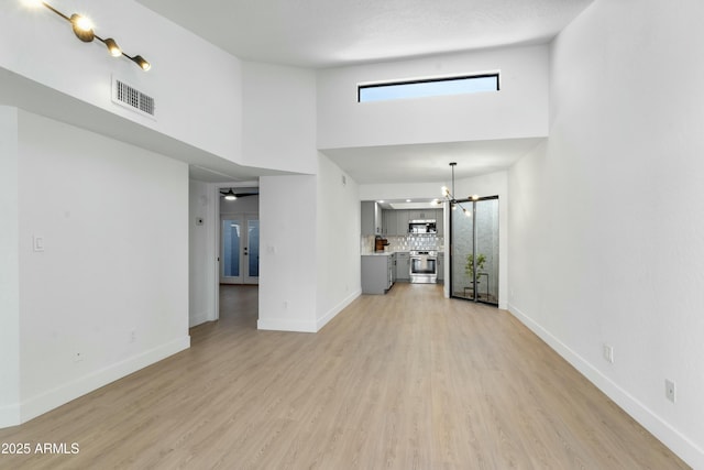 unfurnished living room featuring ceiling fan with notable chandelier, light hardwood / wood-style floors, and a towering ceiling