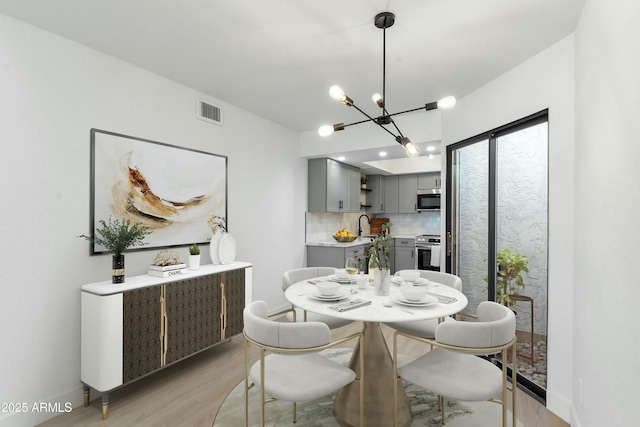 dining space featuring an inviting chandelier, sink, and light hardwood / wood-style flooring