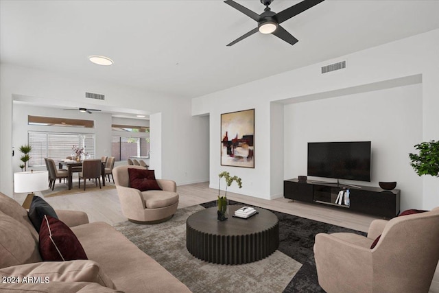 living area with light wood finished floors, ceiling fan, visible vents, and baseboards