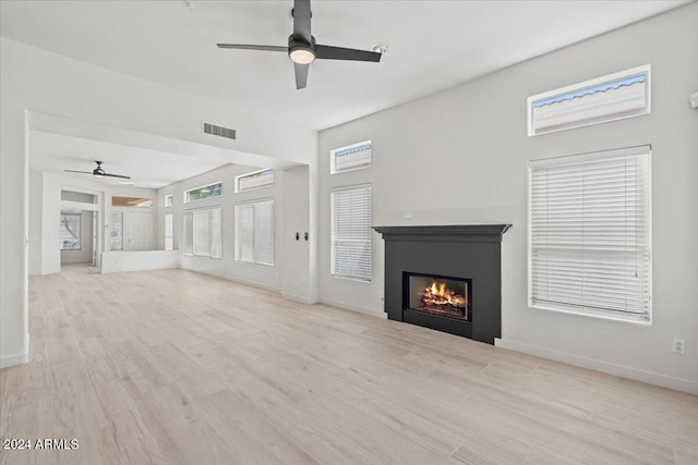 unfurnished living room with light wood-type flooring, visible vents, ceiling fan, and a lit fireplace