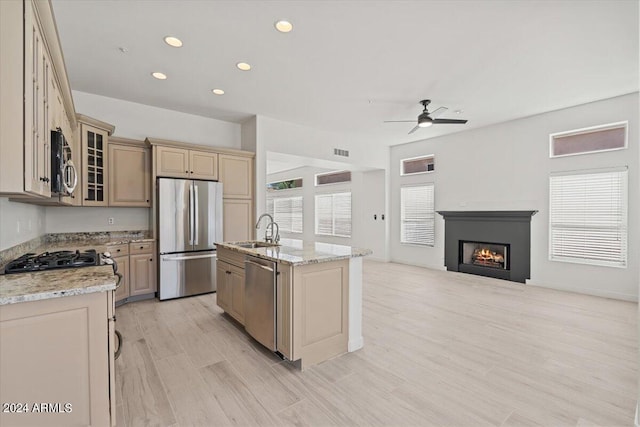 kitchen featuring glass insert cabinets, appliances with stainless steel finishes, open floor plan, a sink, and an island with sink