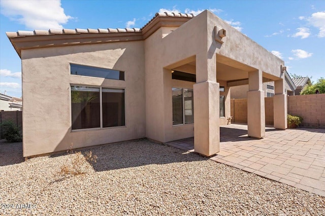 rear view of house with a patio area, fence, and stucco siding