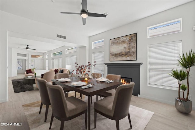 dining room with light wood-style floors, a warm lit fireplace, visible vents, and a healthy amount of sunlight