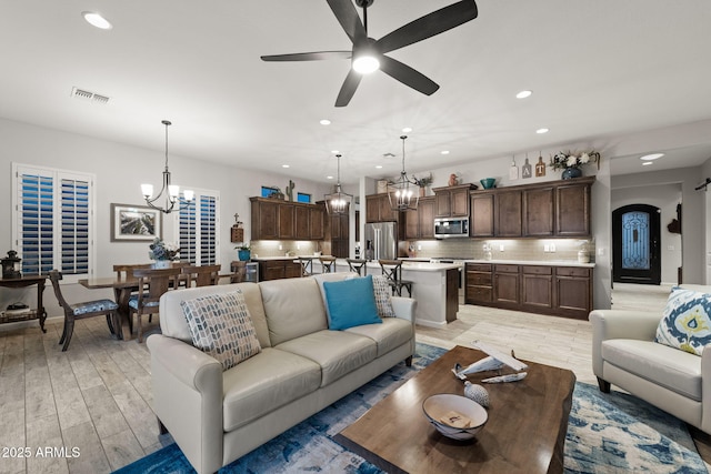 living area featuring arched walkways, recessed lighting, ceiling fan with notable chandelier, visible vents, and light wood-style floors