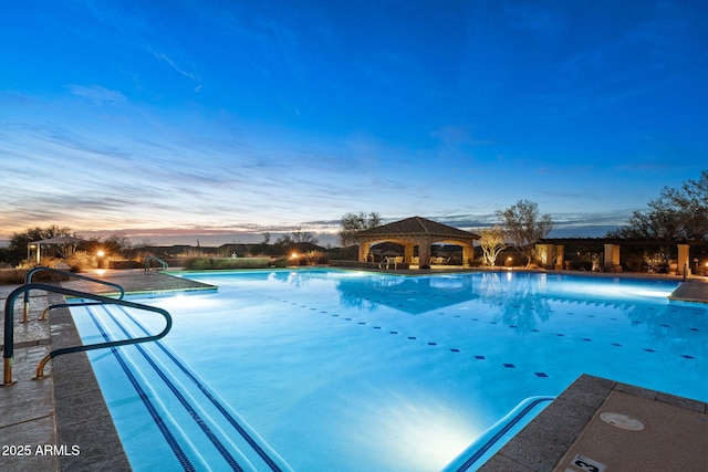 pool at dusk with a gazebo and a community pool