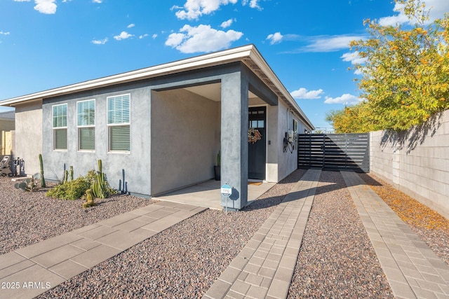 view of side of home with a gate, fence, and stucco siding