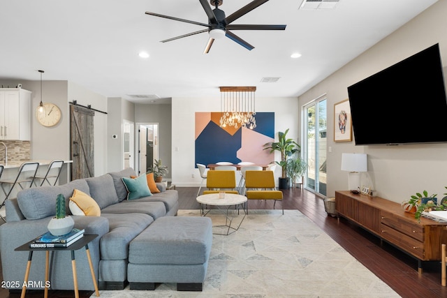 living area featuring a barn door, recessed lighting, visible vents, wood finished floors, and ceiling fan with notable chandelier