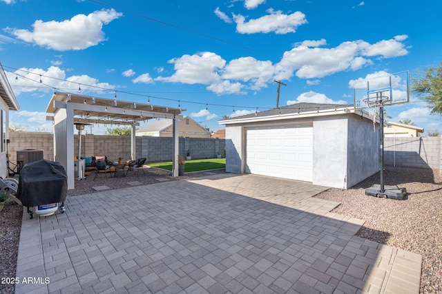 view of patio / terrace with a fenced backyard, a detached garage, an outbuilding, decorative driveway, and central AC