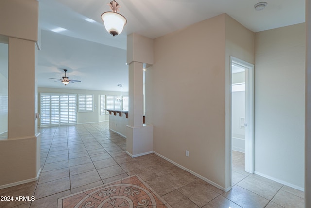 hall with decorative columns, baseboards, and light tile patterned floors