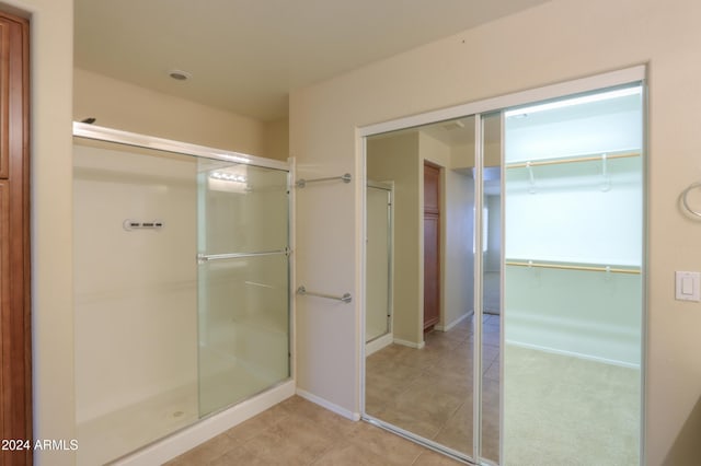 bathroom with tile patterned floors, a shower stall, a walk in closet, and baseboards